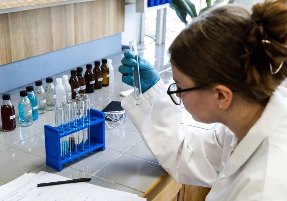 Chemijos laboratorijoje moksleiviai atlieka laboratorinį darbą, naudodami mėgintuvėlius, reagentus ir laboratorinę įrangą.